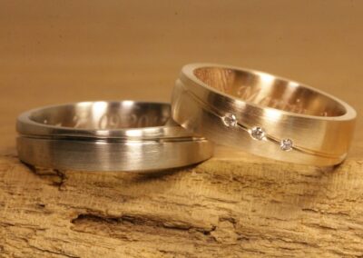 Trauringe aus Gold mit Nut, ein Ring aus Graugold, andere aus Rosegold, in Rosegold Ring drei Brillanten, mit Laser Gravur, Fingerabdruck und Schrifttypo