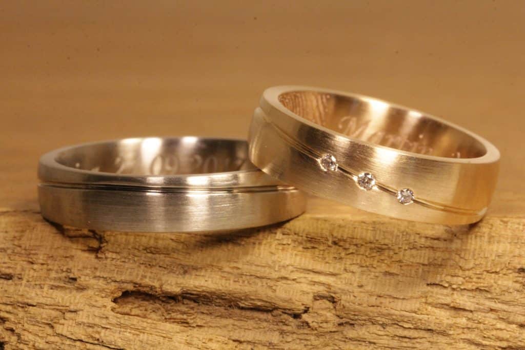 Trauringe aus Gold mit Nut, ein Ring aus Graugold, andere aus Rosegold, in Rosegold Ring drei Brillanten, mit Laser Gravur, Fingerabdruck und Schrifttypo